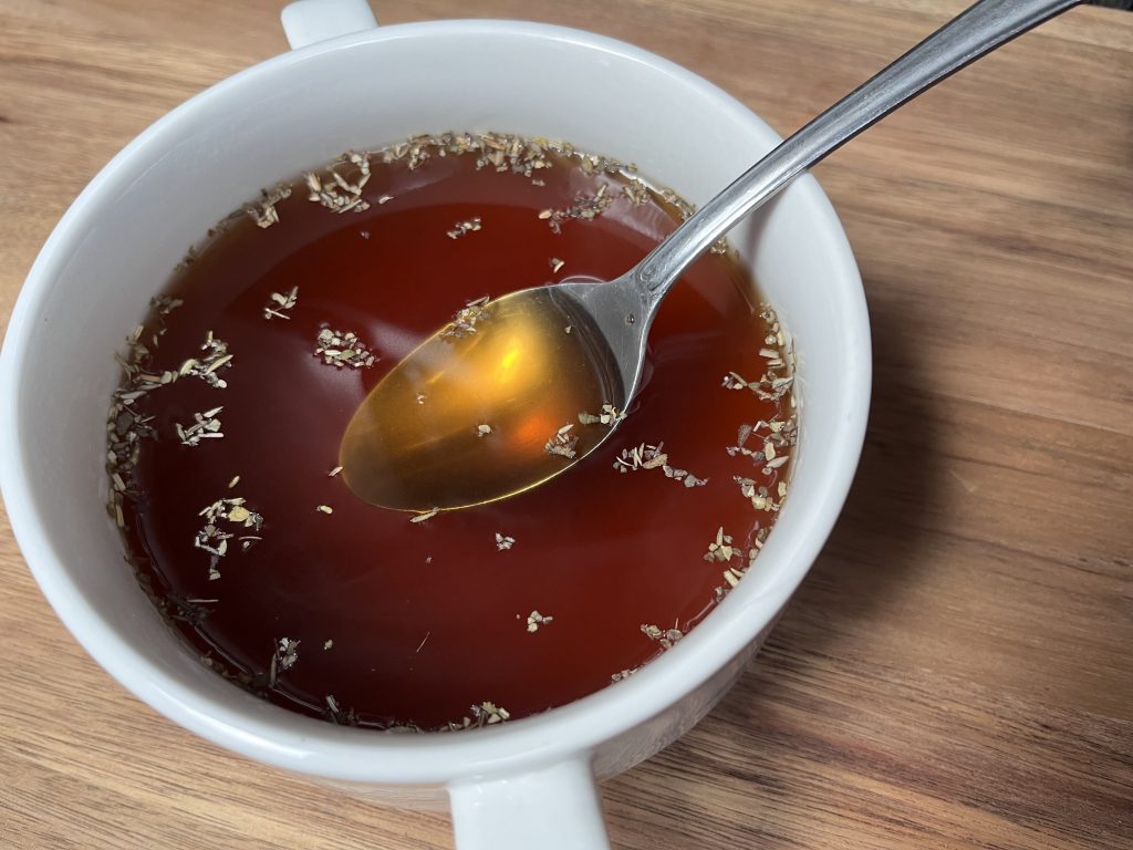 bowl of bone broth with a spoon and seasonings floating on top