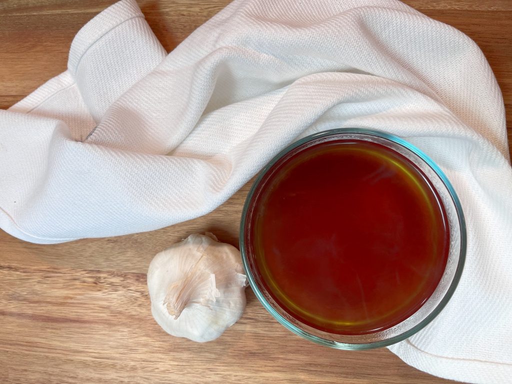 bowl of bone broth next to garlic and white towel