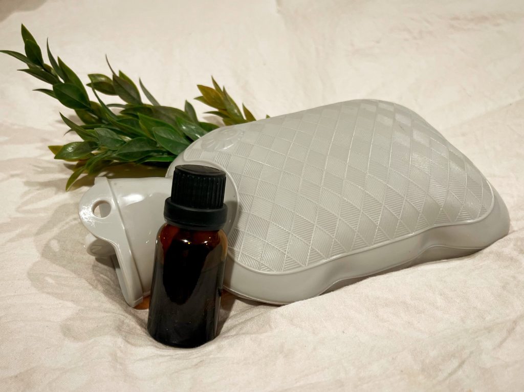 hot water bottle and a bottle of essential oil used to ease the symptoms of PMS